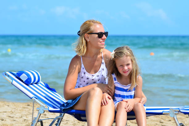 une mère et une petite fille sont assises sur une chaise longue sur la plage - outdoor chair furniture travel vacations photos et images de collection