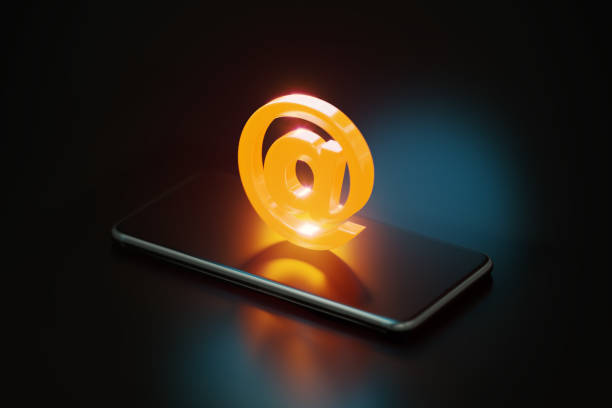 Yellow at symbol glowing over a smart phone on black background. Horizontal composition with copy space.
