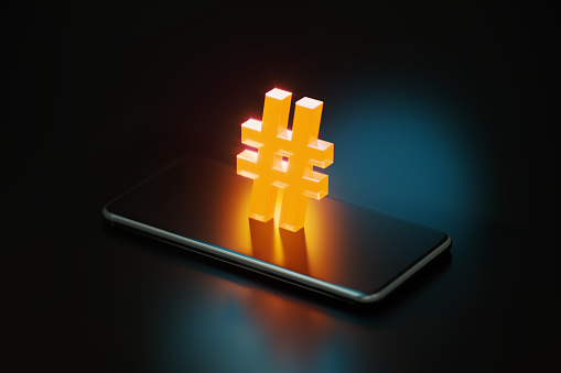 Yellow hashtag symbol glowing over a smart phone on black background. Horizontal composition with copy space.