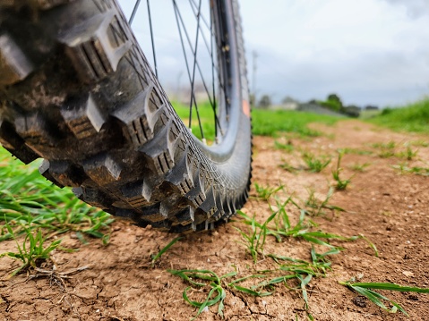 Close up of bicycle tire on dirt road with green grass background.