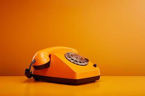 Old fashioned vintage telephone. Orange retro phone against orange background