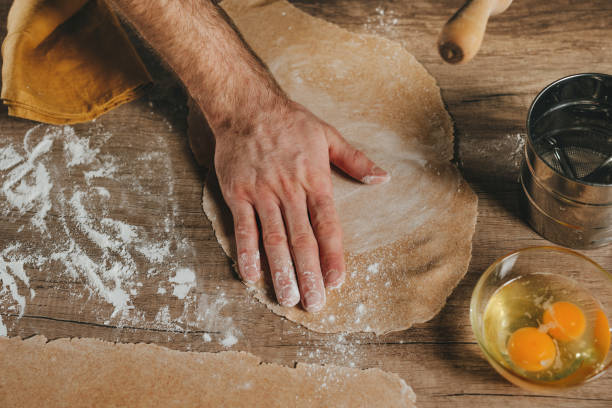 istock Unrecognizable man sprinkling flour on dough rolled out with a rolling pin on a wooden background 1481465984