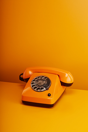 Old fashioned orange vintage telephone. Orange retro phone on orange background