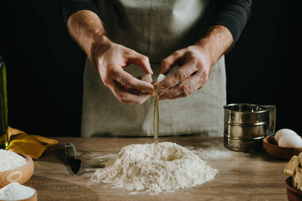 Unrecognizable man kneading dough on wooden background against dark wall