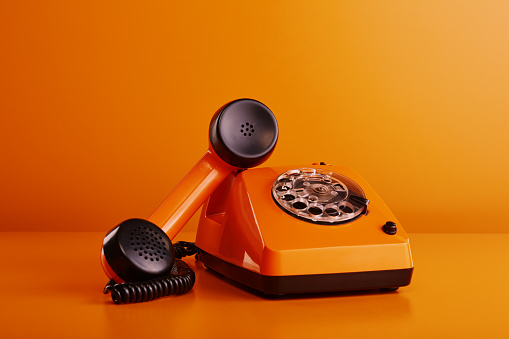 Old fashioned orange vintage telephone. Orange retro phone against orange background