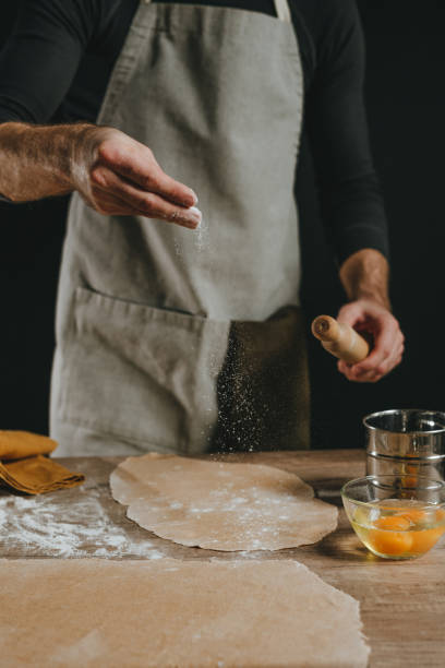istock Unrecognizable man sprinkles flour on dough rolled out with a rolling pin on a wooden background 1481466323