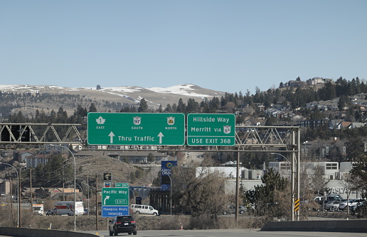 Kamloops, Canada - March 30, 2023: Highway traffic heads to Kamloops via the Trans-Canada 1,  97 and Yellowhead 5. Background shows the hillside Aberdeen neighbourhood. Spring afternoon with clear skies in the Thompson-Nicola Regional District.