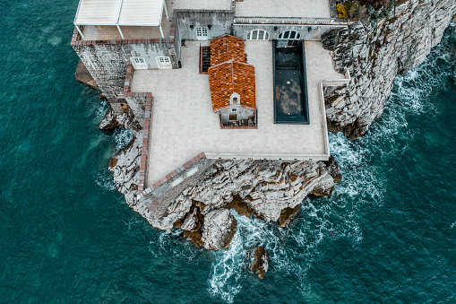 Sveti Stefan island and its small church uniquely located in the middle of the terrace of this iconic place captured with a drone directly from above while emerald water of the Adriatic sea is splashing the island.