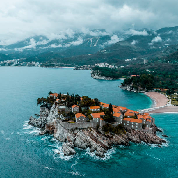 Beautiful and unique Sveti Stefan island in Montenegro seen from a drone perspective during one cloudy spring day and with Budva city in the background.