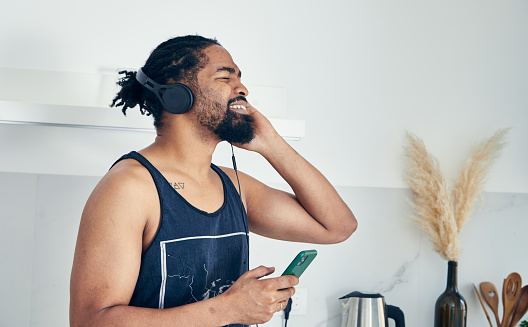 Happy fit black man with a beard and headphones, at home, dressed in casual style for training, meditation or yoga, enjoying music from the smartphone, representing freedom, joy, fulfillment and leisure lifestyle, wellbeing and indulgence in music, an image with a copy space