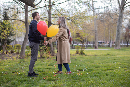 Beautiful young couple are enjoying in the public park. They are smiling and holding balloons.