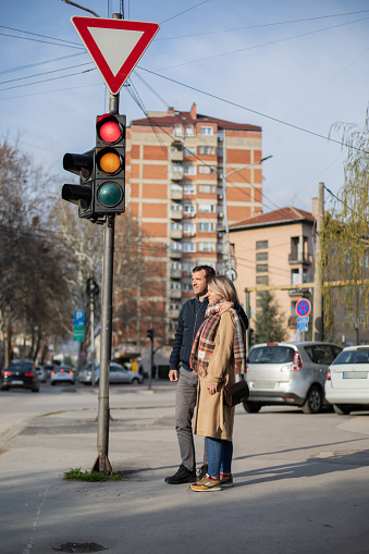 Beautiful young couple are walking through the city. They are waiting to cross the street.