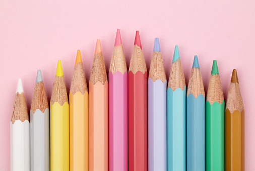 Colored pencils of pastel colors on a pink background. Multi-colored pastel pencils.