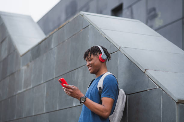 istock Young man with red headphones, smartphone and a notebook leaning against the wall. 1481492938
