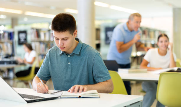 istock Focused casual young male writing in planner and using laptop in the library 1481493962