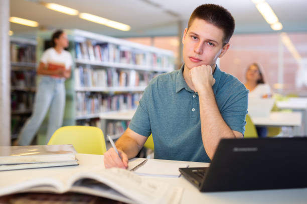 istock Positive young man in casual clothes working remotely using a computer in a quiet library 1481494086