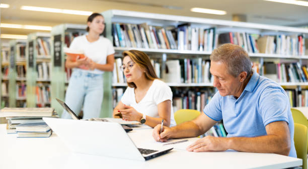 istock Mature man spending time in library, reading books and making laptop. Self-education concept 1481494322