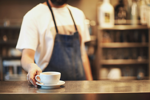 Close up of male barista serving cup of fresh coffee. Cup of coffee in the hands of waiter.