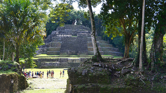 Wide shot of tourists dwarfed by the Temple of the Jaguar Mayan pyramid in Lamanai, Belize