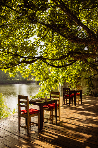 Dinning tables at the romantic restaurant on patio by the lake under a tree.