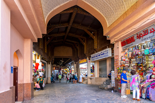 View from the streetside arched entrance as local Omanis and tourists shop inside the historic Mutrah Souk, or Souq,  a long-running, old-fashioned bazaar featuring household goods, clothing, spices, antiques & more, located on the waterfront Corniche in Muscat, Oman.