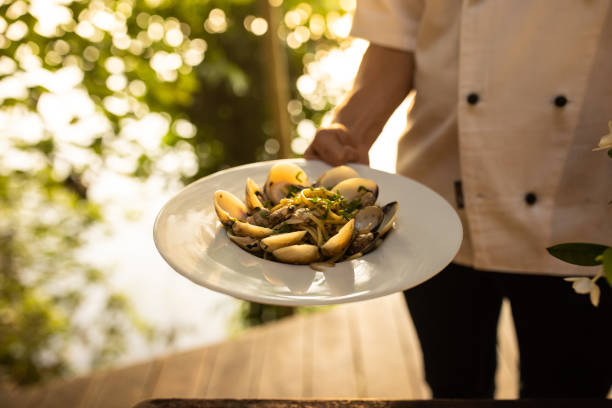 Male waiter holding tasty pasta meal with clams  at the restaurant outdoors.