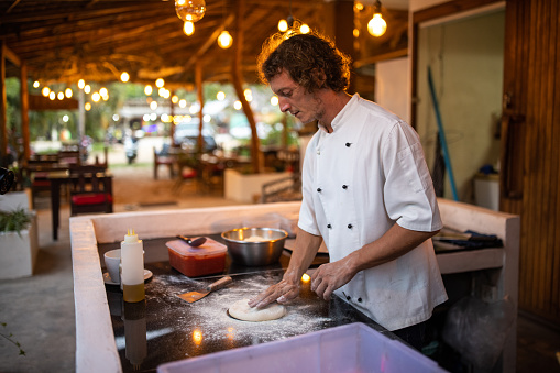 Male chef preparing dough for pizza in restaurant kitchen.