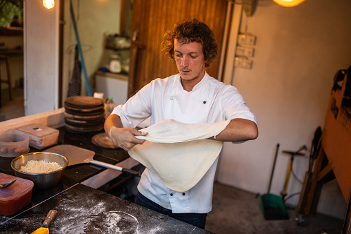 Male chef preparing dough for pizza in restaurant kitchen.