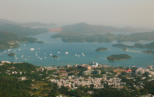 Bird's-eye view of a seaside town surrounded by greenery and blue sea with numerous yaughts and clusters of islands off shore