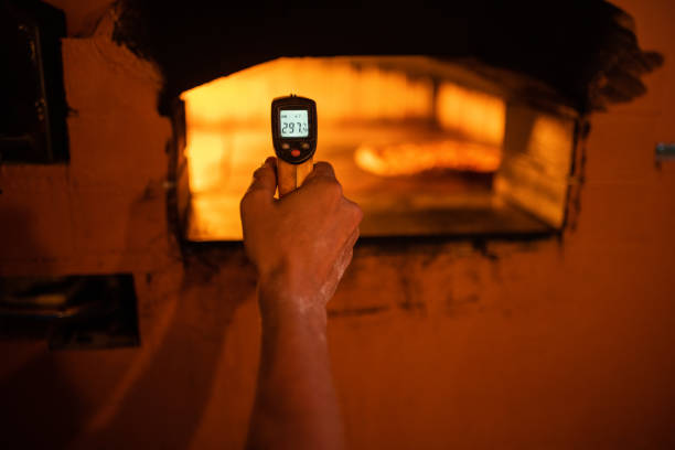 Italian male chef measuring temperature in traditional pizza oven in restaurant kitchen.