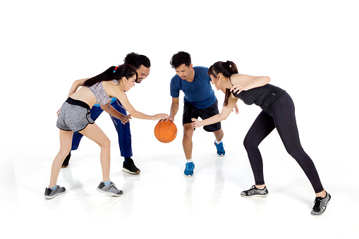 Group of young people bouncing basketball while training session together in the studio. Isolated on white background