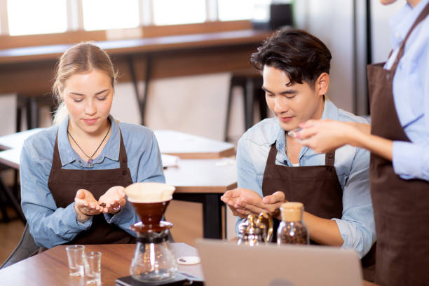 Young man and woman learning making coffee and sniff bean with barista while laptop on desk at cafe, group people training drip coffee with entrepreneur, small business or SME. stock photo