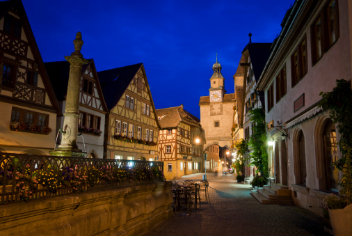 Rothenburg ob der Tauber,  medieval, picturesque town, Germany, at  twilight. Roederbrunnen in foreground. Traditional gable houses flank the road to Roeder Arch (Roderbogen) and  Markus Tower (Markusturm).