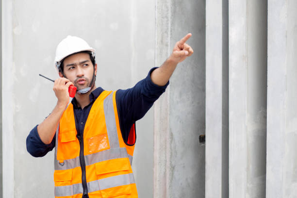Young man engineer using radio command with worker in construction site, architect or contractor speak to radio for control and planning development structure at precast factory, industrial concept. joven ingeniero que utiliza el comando de radio con el trabajador en el sitio de construcción, arquitecto o contratista habla con la radio para el control y la planificación de la estructura de desarrollo en la fábrica de prefabricados, concepto industr