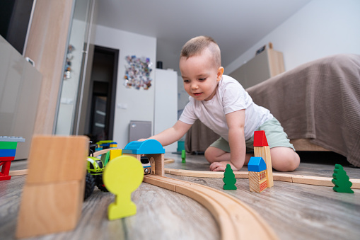 Joyful baby playing toy railroad on the floor of domestic room.