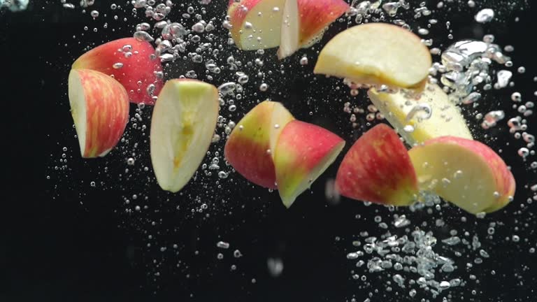 Many Pieces Of Ripe Apples Falling Into Water On The Black Background