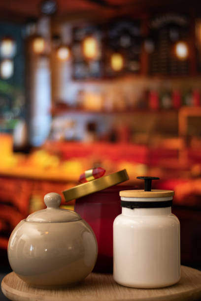 Vertical view of Mugs of sugar and salt containers style vintage over a table in night restaurant with selective focus and bokeh background Vertical view of Mugs of sugar and salt containers salt pepper ingredient black peppercorn stock pictures, royalty-free photos & images