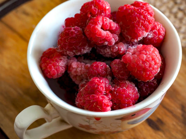 fresh bright frozen raspberries in a cup on the table, macro