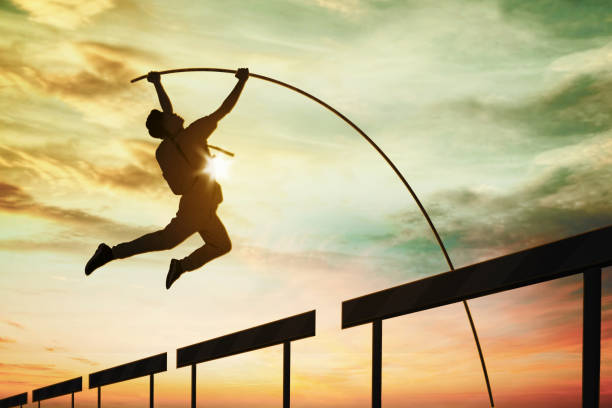 Silhouette of male student jumping through obstacles line while using a stick with dusk sunlight background