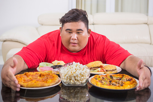 Close up of fat man looks tempted to eat lots of fast food while sitting in the living room at home