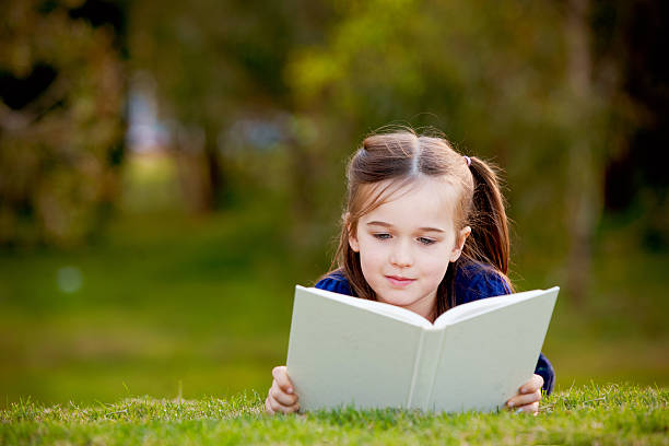 istock Little girl enjoying reading outdoors on the grass 148157235