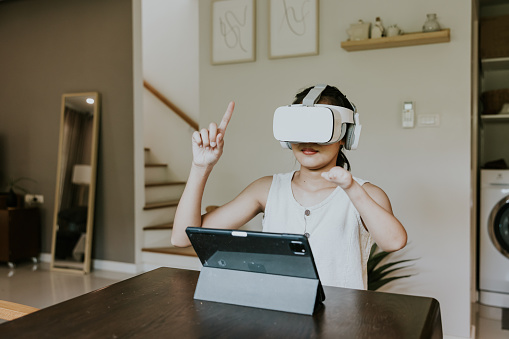 Happy young adult woman enjoy her online class at home, wearing virtual reality simulator and watching display inside.