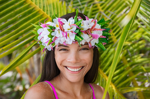 Tahiti flower crown hei po'o smiling woman wearing tahitian headpiece wreath cultural decoration. Bora Bora, French Polynesia. Beauty Asian multiracial model smile on palm tree background.