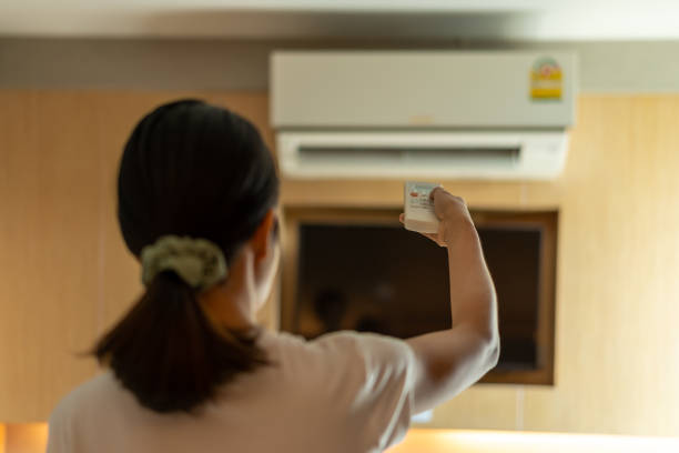istock Asia Woman holding remote control aimed air conditioner. 1481582843