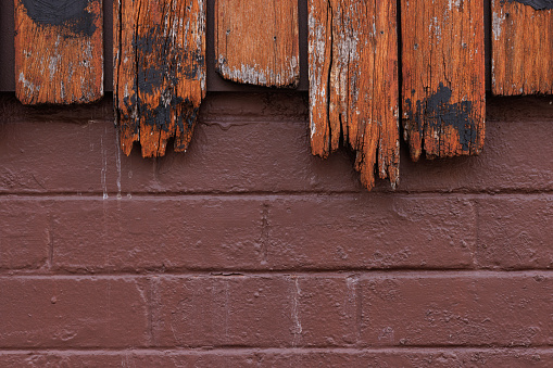 Close-up on part of a brown brick wall underneath an old rotting and stained wooden fence.