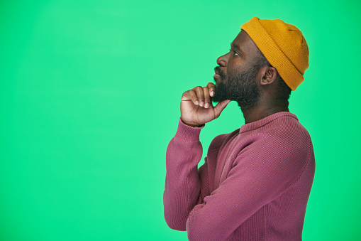 Side view of African American man in yellow hat loooking away with pensive expression against green background