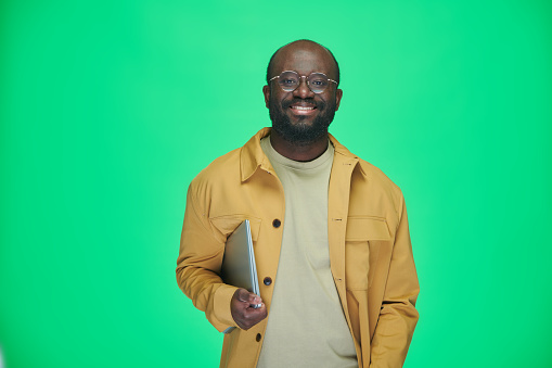 Portrait of African American man in eyeglasses with digital tablet smiling at camera on green background