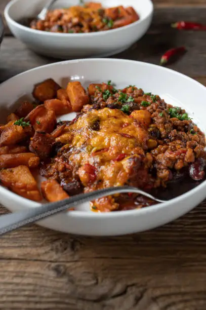 Delicious and savory bean stew, mexican and tex mex style. Cooked with kidney beans, baked beans, ground beef, tomatoes, chili, peppers, onion, garlic and herbs. Gratinated with cheddar cheese and served with roasted sweet potatoes on a plate