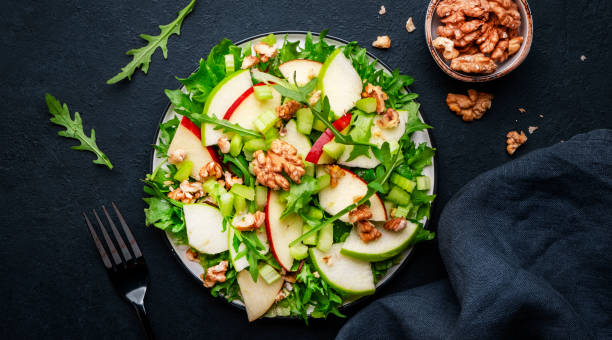 istock Waldorf salad with red and green apple, celery, lettuce, arugula and walnuts on plate, black table background, top view 1481601093