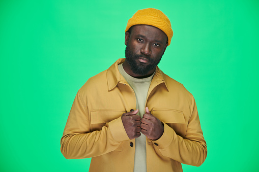 Portrait of African American man in yellow hat and jacket looking at camera on green background